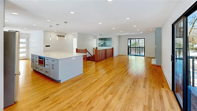 kitchen with a kitchen island, pendant lighting, stainless steel refrigerator, gray cabinetry, and light hardwood / wood-style floors