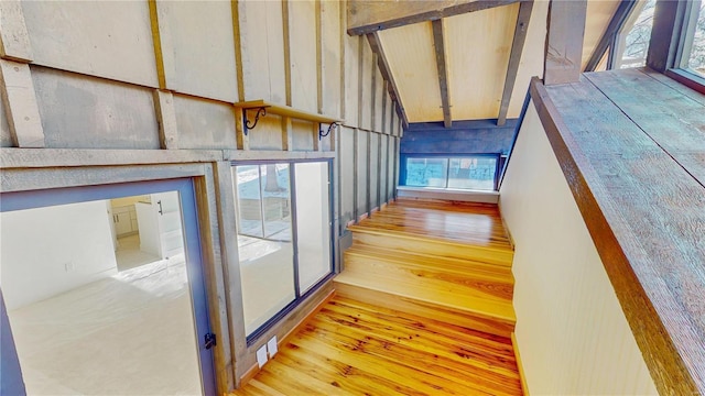 stairway with lofted ceiling with beams, a healthy amount of sunlight, and hardwood / wood-style floors