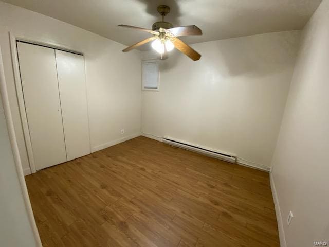 unfurnished bedroom featuring wood-type flooring, a baseboard heating unit, ceiling fan, and a closet