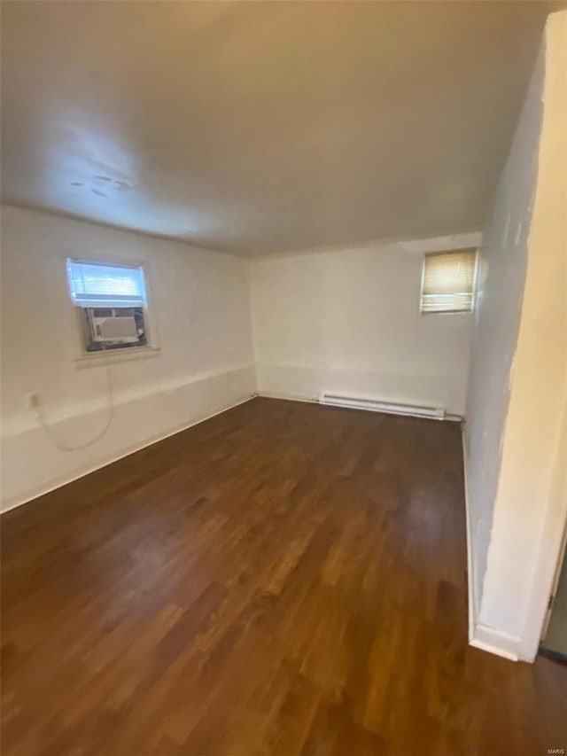 basement with a baseboard heating unit, cooling unit, and dark hardwood / wood-style flooring