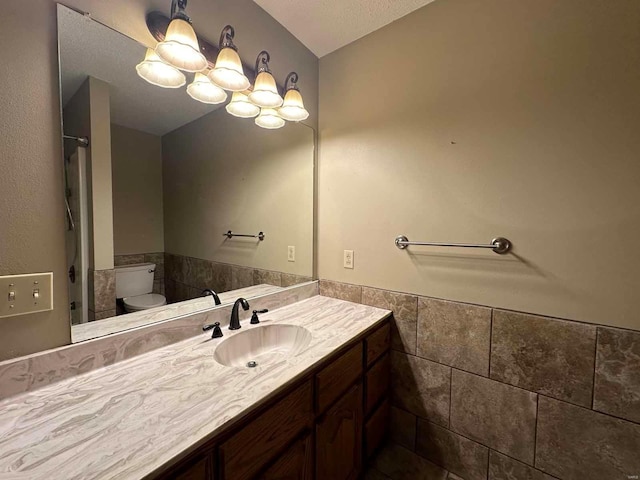 bathroom with toilet, an inviting chandelier, tile walls, a textured ceiling, and vanity