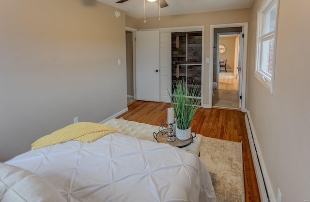 bedroom with ceiling fan, a baseboard radiator, light hardwood / wood-style floors, and a closet