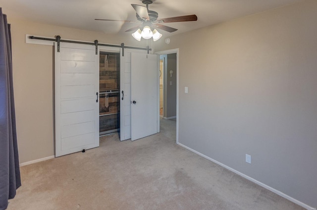 unfurnished bedroom featuring ceiling fan, light colored carpet, and a barn door