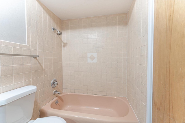 bathroom featuring tiled shower / bath, toilet, and tile walls