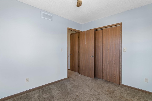 unfurnished bedroom featuring ceiling fan, a closet, a textured ceiling, and carpet flooring