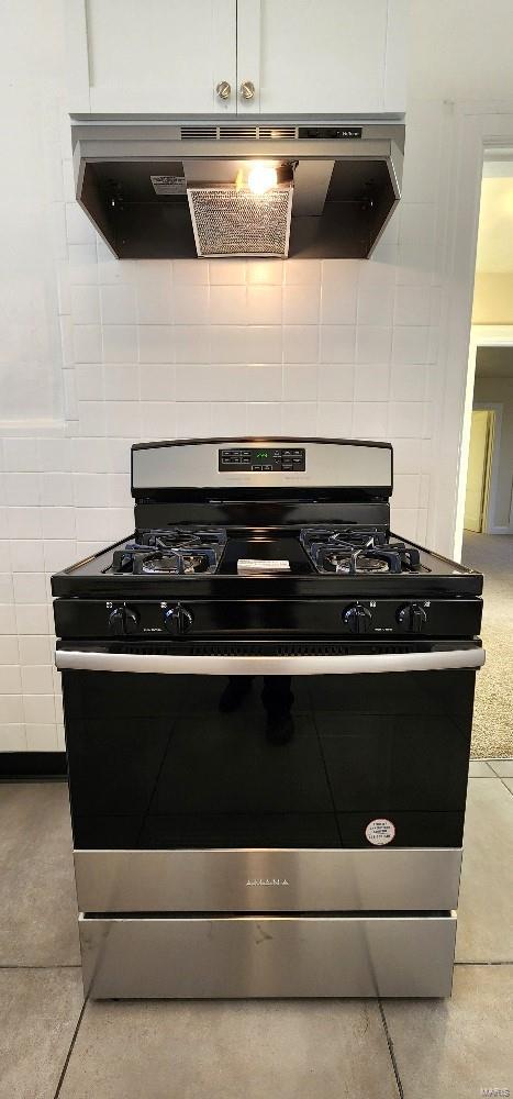 kitchen featuring backsplash, stainless steel gas range oven, tile patterned floors, and white cabinets