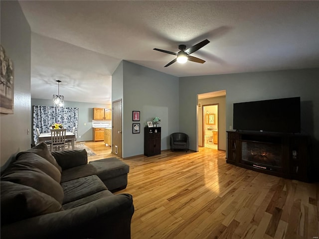 living room with light wood-style floors, ceiling fan, a fireplace, and vaulted ceiling