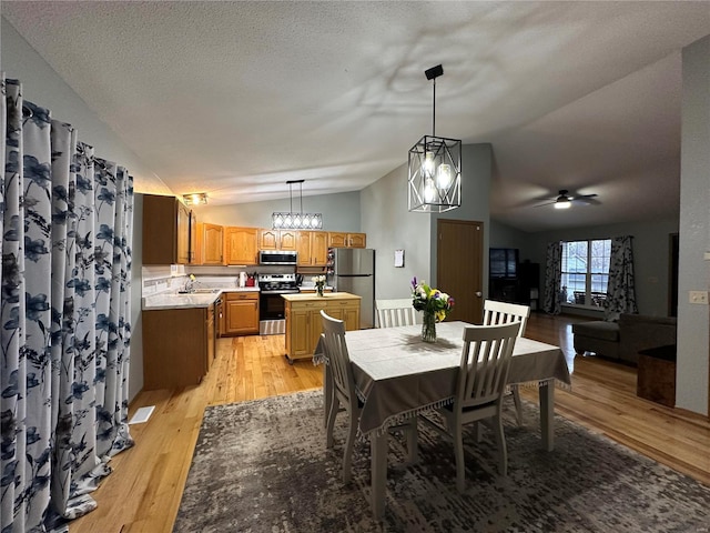 dining area with lofted ceiling, light wood-style flooring, ceiling fan, and a textured ceiling