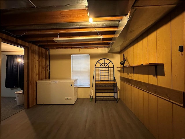 unfinished below grade area featuring refrigerator, wooden walls, and wood finished floors