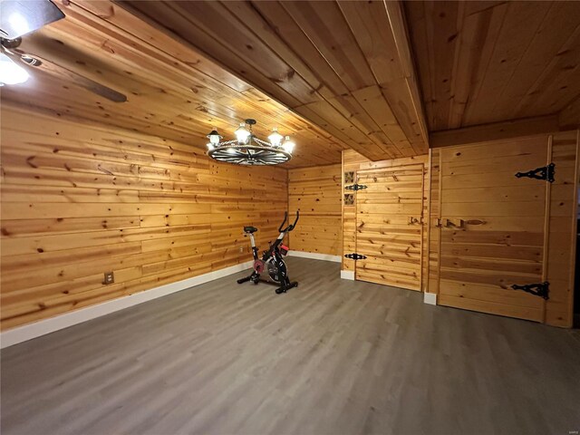 exercise area featuring wooden walls, baseboards, wooden ceiling, wood finished floors, and a chandelier