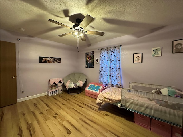 bedroom with a textured ceiling, light wood-type flooring, a ceiling fan, and baseboards