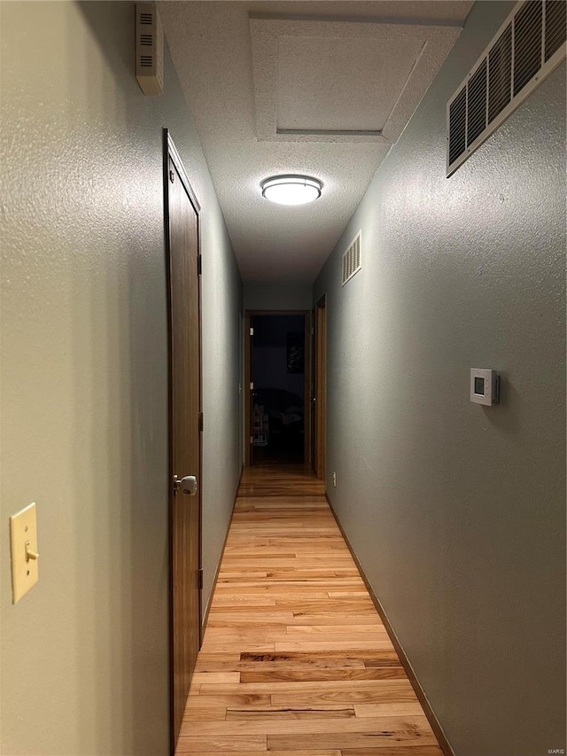 corridor with light wood-type flooring, attic access, visible vents, and a textured ceiling