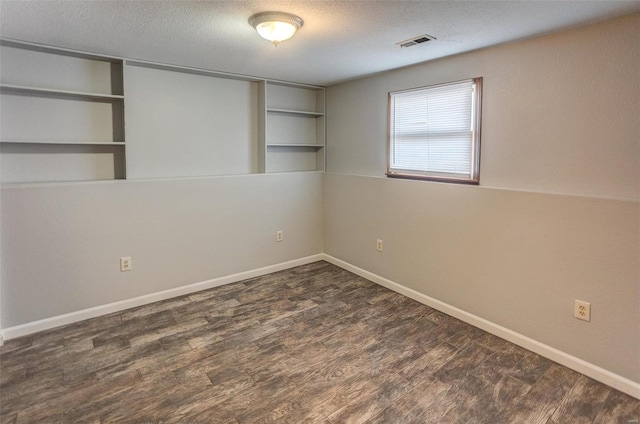 empty room with dark hardwood / wood-style flooring, built in features, and a textured ceiling