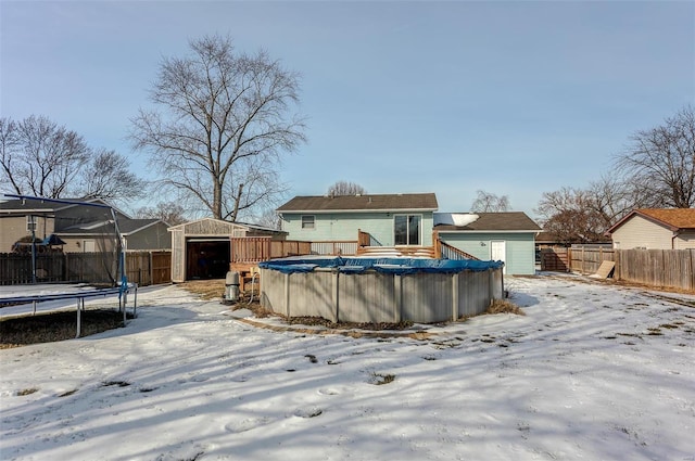 snow covered property featuring a trampoline, a covered pool, and a storage unit