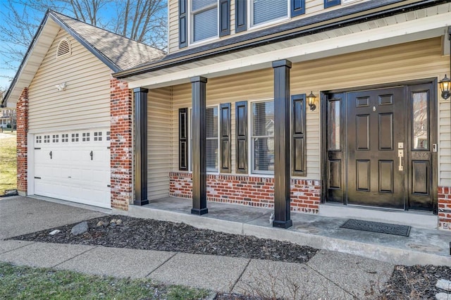 view of exterior entry featuring brick siding, a shingled roof, covered porch, a garage, and driveway