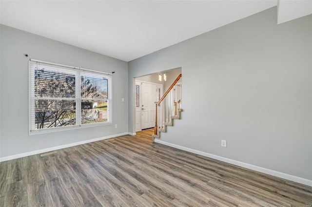 empty room with stairs, wood finished floors, visible vents, and baseboards