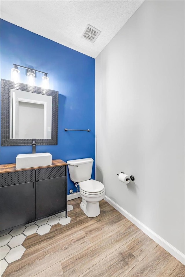 bathroom featuring visible vents, toilet, a textured ceiling, wood finished floors, and baseboards