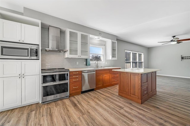 kitchen with wall chimney exhaust hood, appliances with stainless steel finishes, wood finished floors, light countertops, and a sink