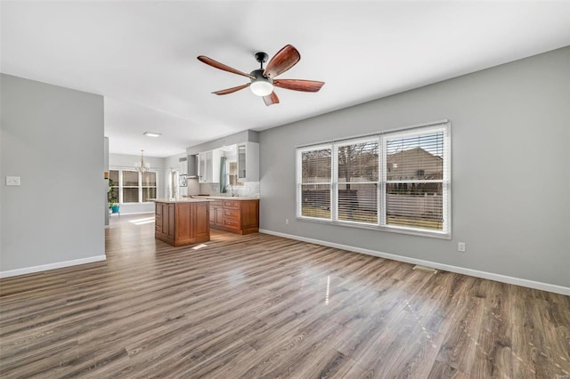 unfurnished living room featuring baseboards, wood finished floors, and ceiling fan with notable chandelier