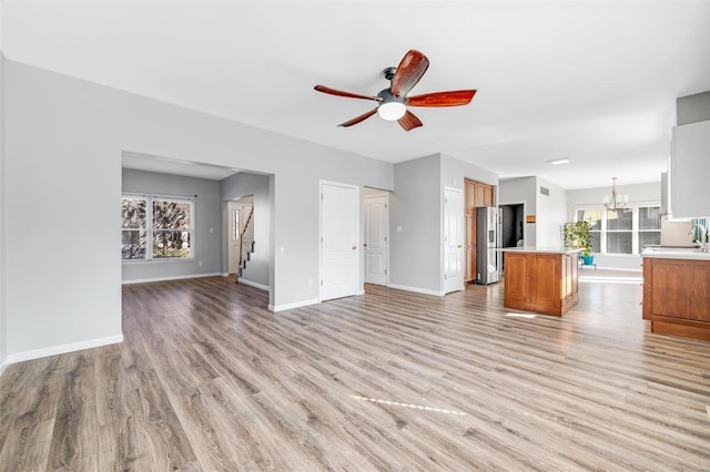 unfurnished living room featuring light wood-style floors, baseboards, a sink, and ceiling fan with notable chandelier