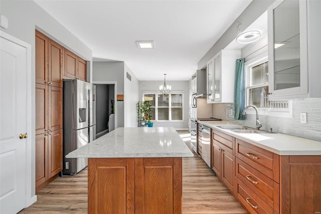 kitchen featuring a kitchen island, appliances with stainless steel finishes, glass insert cabinets, light wood-type flooring, and a sink