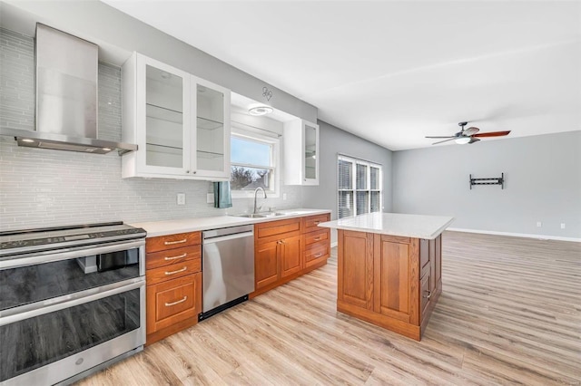 kitchen with decorative backsplash, wall chimney exhaust hood, stainless steel appliances, light countertops, and a sink