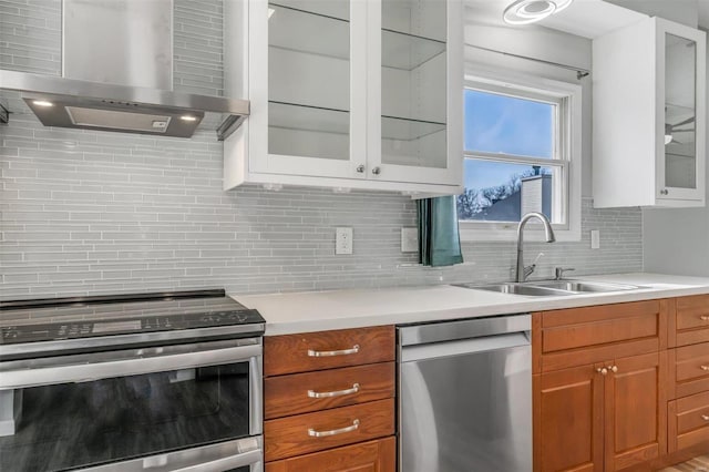 kitchen featuring stainless steel appliances, a sink, light countertops, wall chimney range hood, and decorative backsplash