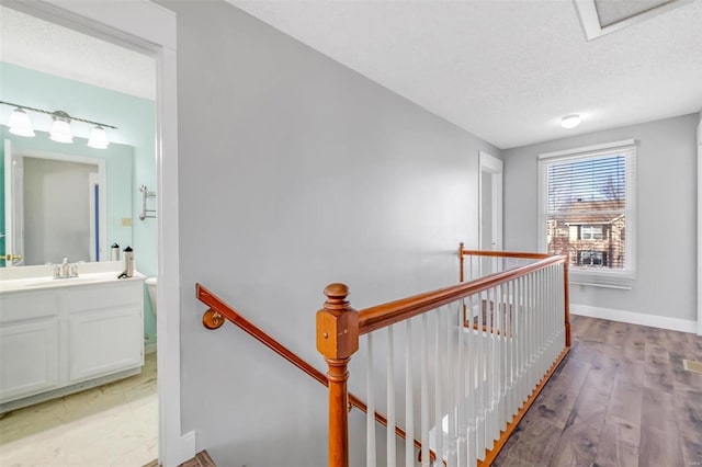 hall with a textured ceiling, baseboards, an upstairs landing, and light wood-style floors