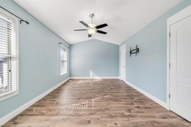 empty room with lofted ceiling, ceiling fan, wood finished floors, and baseboards