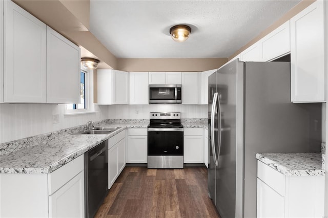 kitchen with sink, white cabinetry, appliances with stainless steel finishes, dark hardwood / wood-style flooring, and light stone countertops