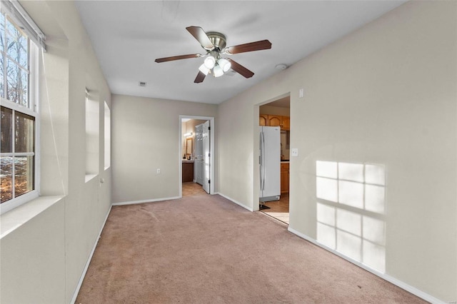 unfurnished bedroom featuring connected bathroom, light carpet, white fridge, ceiling fan, and multiple windows