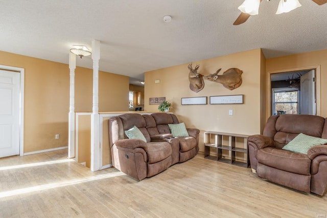 living area with light wood-style floors, baseboards, a ceiling fan, and a textured ceiling