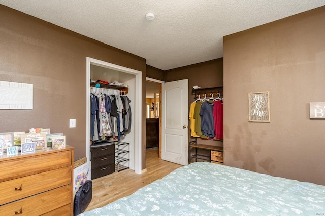 bedroom with a textured ceiling, a spacious closet, a closet, and light wood-style flooring