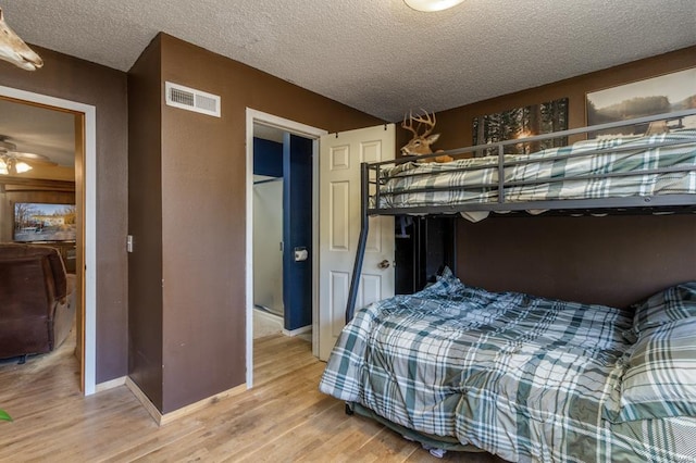 bedroom featuring baseboards, visible vents, a textured ceiling, and light wood finished floors