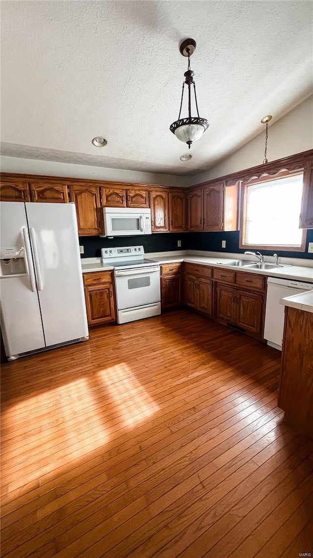 kitchen featuring vaulted ceiling, pendant lighting, sink, light hardwood / wood-style floors, and white appliances