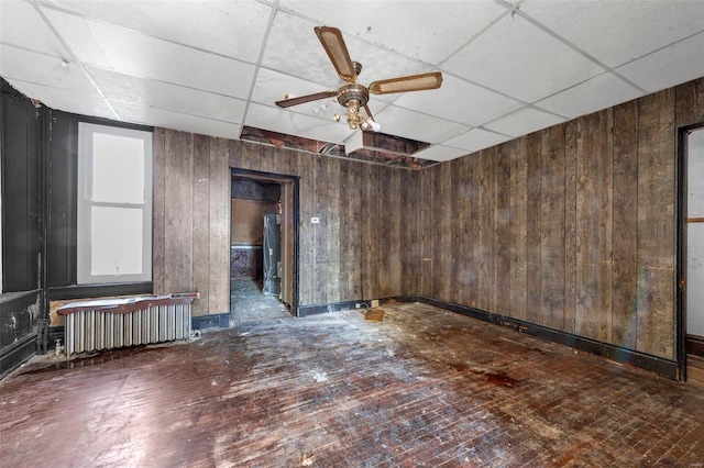 spare room with radiator, a paneled ceiling, ceiling fan, wooden walls, and dark hardwood / wood-style floors