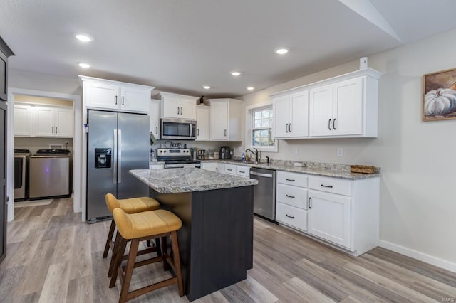 kitchen featuring white cabinetry, a center island, separate washer and dryer, a kitchen breakfast bar, and stainless steel appliances