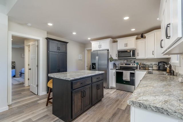 kitchen with sink, light wood-type flooring, appliances with stainless steel finishes, a kitchen island, and white cabinets