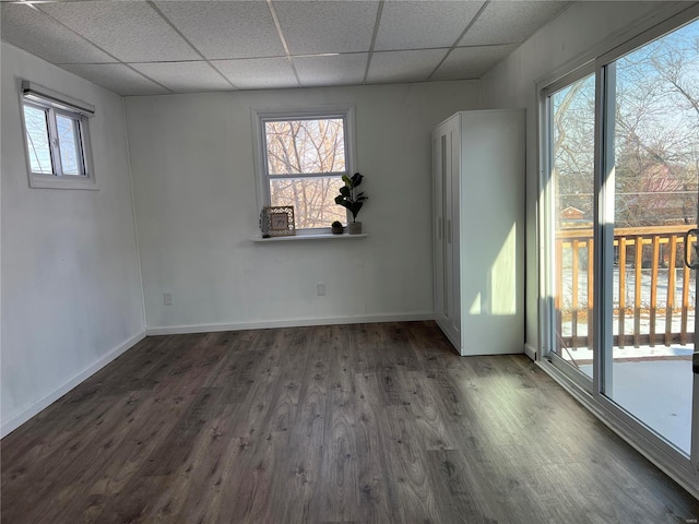 empty room with dark wood-type flooring, a paneled ceiling, and plenty of natural light