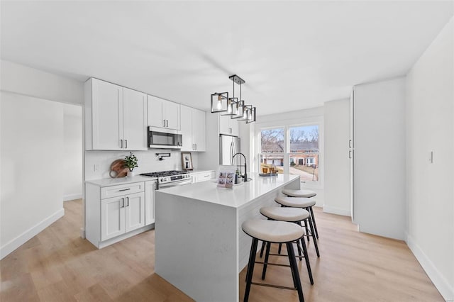 kitchen with white cabinetry, decorative light fixtures, an island with sink, stainless steel appliances, and backsplash