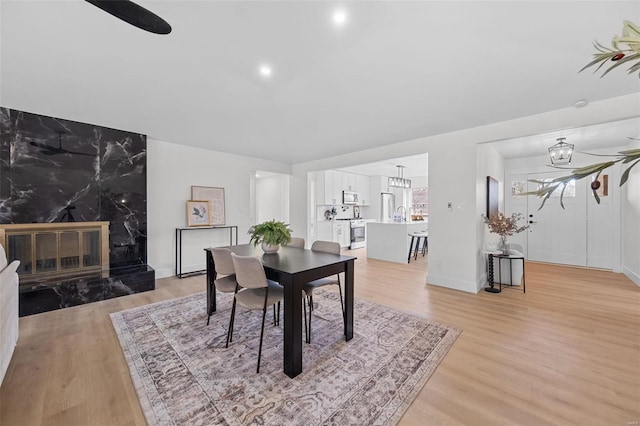 dining area featuring a premium fireplace, a chandelier, and light wood-type flooring