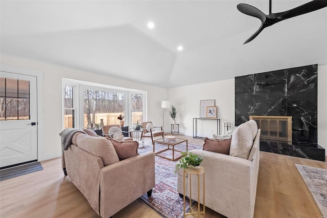 living room featuring vaulted ceiling, a premium fireplace, ceiling fan, and light wood-type flooring