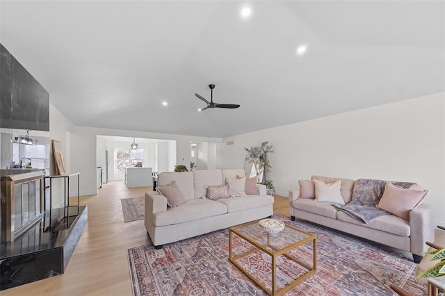 living room featuring lofted ceiling, ceiling fan with notable chandelier, and light hardwood / wood-style flooring