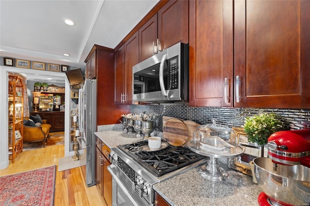 kitchen with appliances with stainless steel finishes, stone countertops, light hardwood / wood-style floors, and decorative backsplash