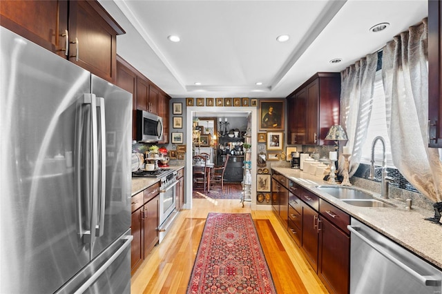 kitchen featuring sink, stainless steel appliances, light stone countertops, a raised ceiling, and light wood-type flooring