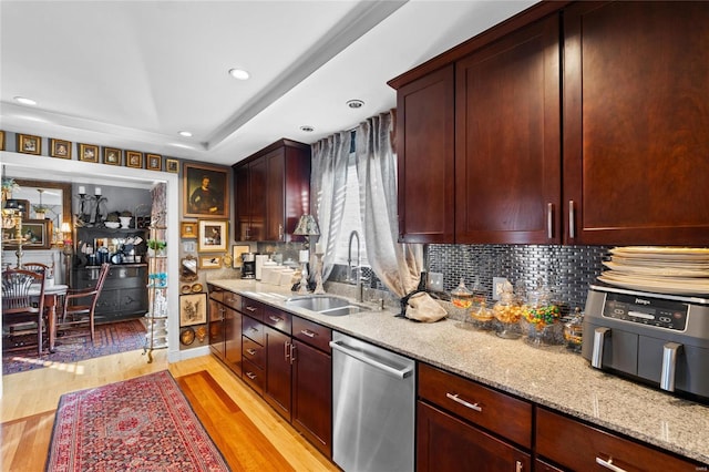 kitchen with sink, tasteful backsplash, light wood-type flooring, stainless steel dishwasher, and light stone countertops