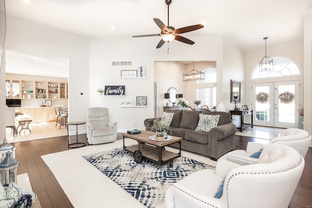 living room featuring ceiling fan with notable chandelier, dark wood-type flooring, and french doors