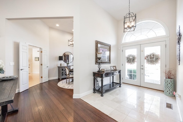 foyer entrance with a towering ceiling, light hardwood / wood-style flooring, an inviting chandelier, and french doors