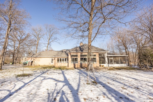 snow covered rear of property featuring a sunroom