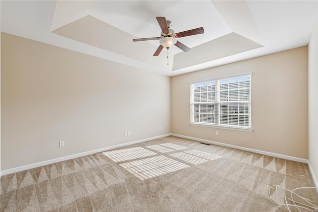 empty room featuring a tray ceiling, light colored carpet, and ceiling fan